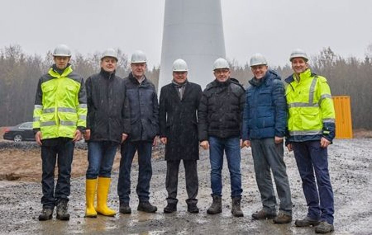 Sieben Männer mit Schutzhelmen stehen vor einem Windrad.