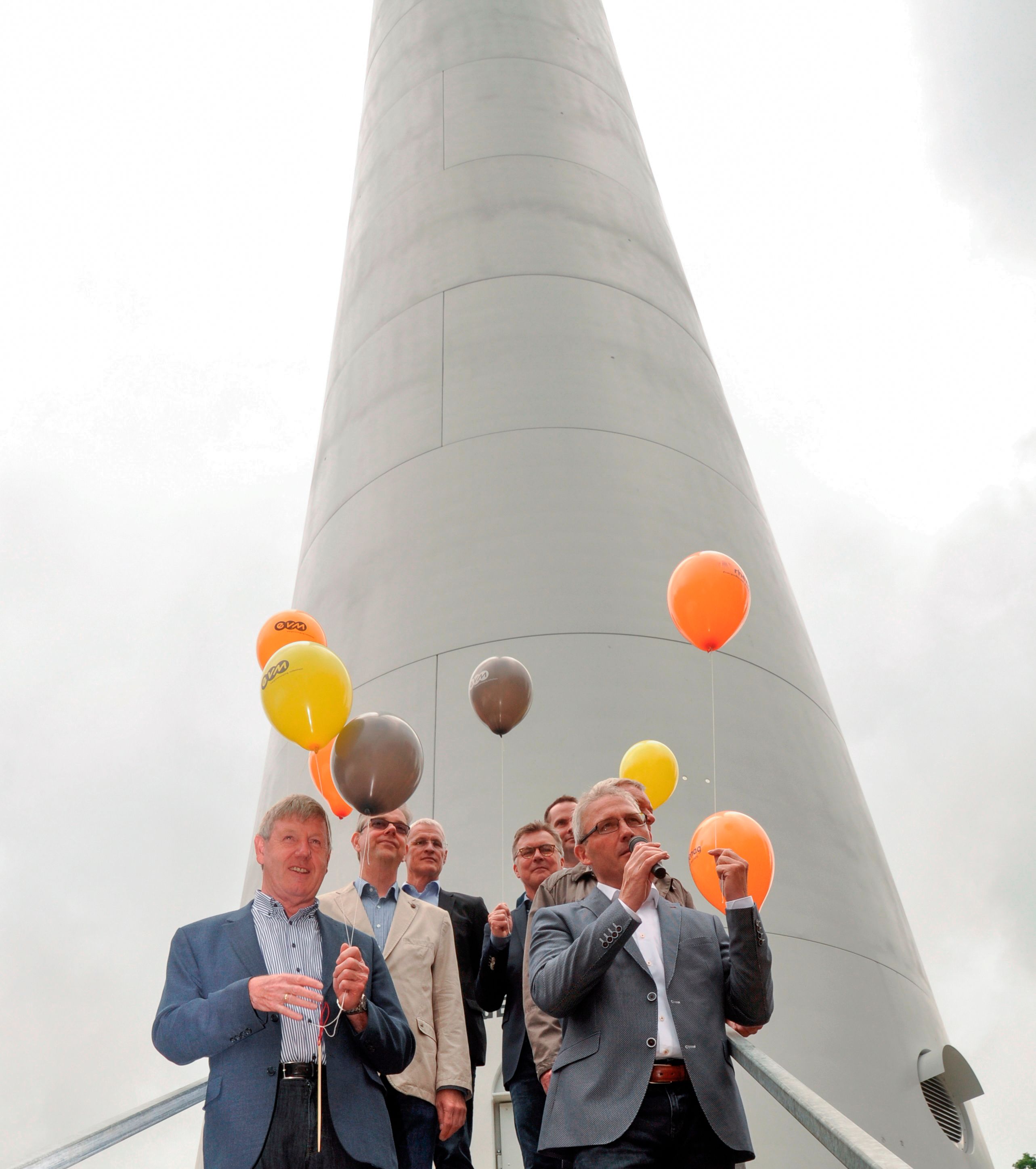 Mehrere Männer stehen mit orangenen Ballons vor einem Windrad